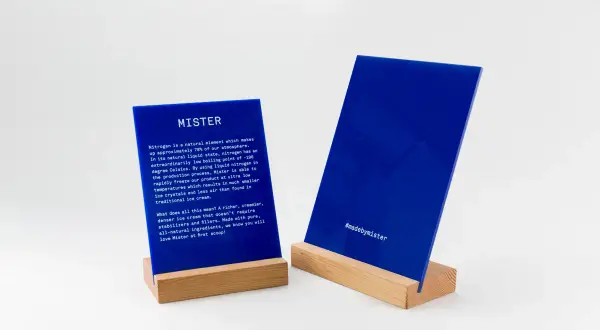 Deux panneaux en **lettre plexiglas** bleus sur des supports en bois. L'un décrit le processus de fabrication de Mister, l'autre affiche le hashtag #madebymister.