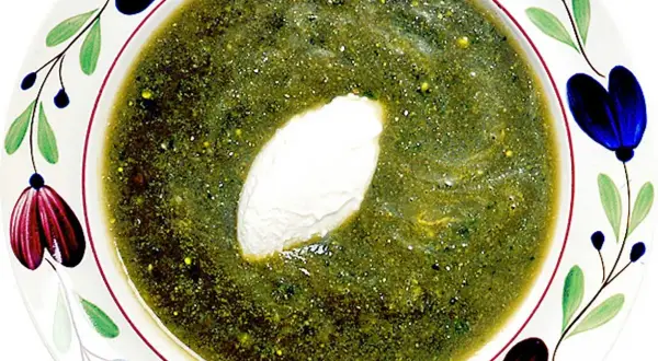 A bowl of green soup with a dollop of cream, garnished with colorful floral patterns.
