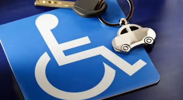 Chiave e portachiavi a forma di auto su un cartello blu con simbolo di disabilità. Possibile riferimento a invalidità civile 75 e bollo auto.