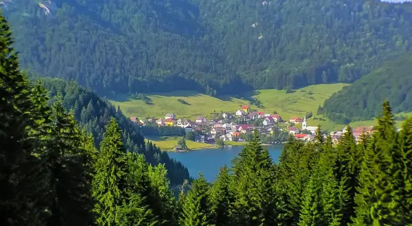 Idyllisches Dorf am See, umgeben von grünen Hügeln und Nadelwäldern. Perfekt für Slowakei Reisetipps!