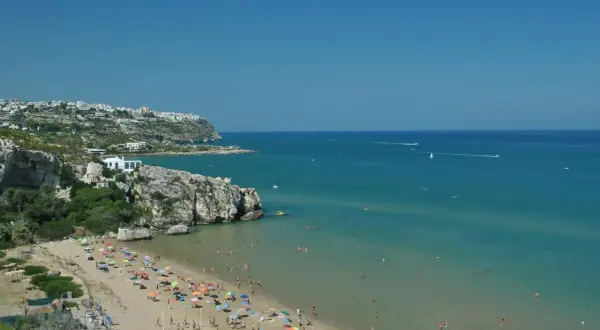 Peschici spiaggia Zaiana, con gente che prende il sole e nuota nelle acque cristalline sotto un cielo azzurro.