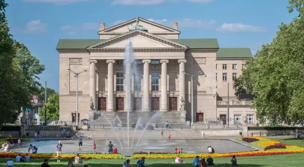 Poznań atrakcje dla dorosłych: Teatr Wielki i fontanny w słoneczny dzień. Ludzie odpoczywają na trawie, ciesząc się miejskim krajobrazem.