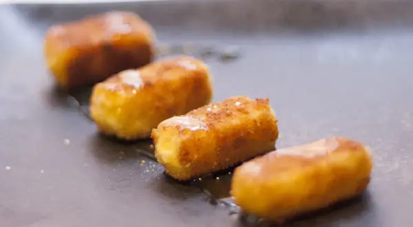 Friterad fetaost i stavar, gyllene och krispiga, serverade på en mörk tallrik med en lätt glasyr.