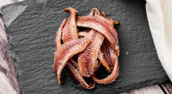 Kupa rybek anchois ułożona na czarnej desce, gotowa do podania.