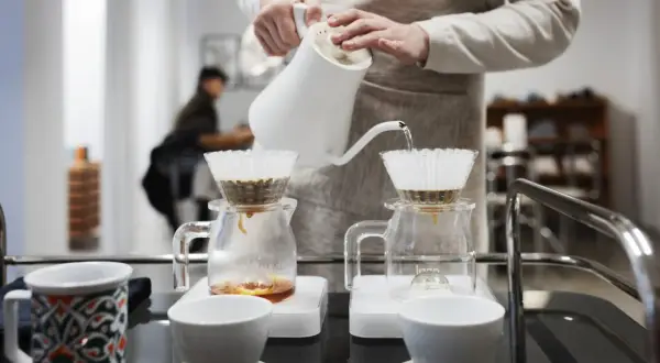 En person häller varmt vatten över kaffefilter för att brygga kaffe. En tanke på vad kostar en kopp kaffe hemma.