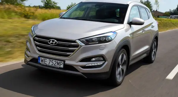 Srebrny Hyundai Tucson 3 jedzie po drodze, otoczony zielenią.