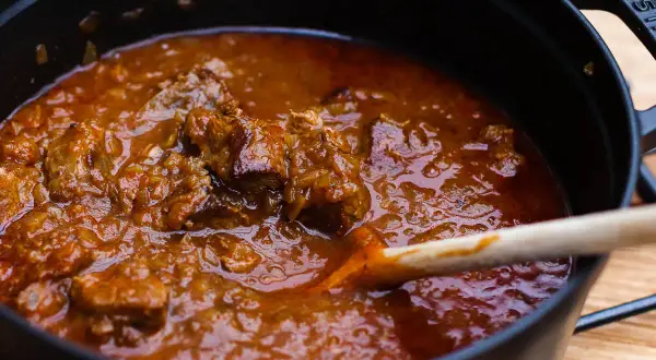 Ein dampfender Topf mit zartem Wiener Saftgulasch, das nach dem Originalrezept zubereitet wurde. Eine Holzschöpfkelle rührt in der köstlichen Sauce.