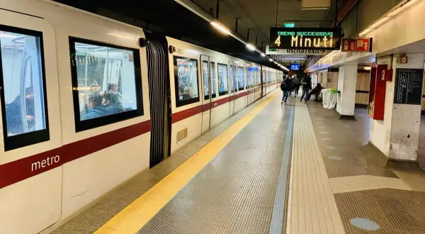 Pasażerowie czekają na peronie na metro we Włoszech. Na tablicy informacyjnej widnieje napis "Treno Successivo 4 Minuti".