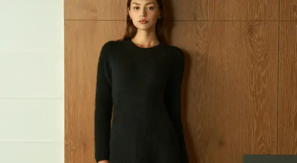 Frau in schwarzem Strickkleid vor Holzvertäfelung. Ein schlichtes Outfit, das zu den modernen Dresscodes für Frauen passt.