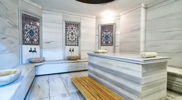 Wnętrze hammamu: marmurowe ściany, ozdobne kafelki, kamienne misy i ława. To miejsce relaksu i odnowy, gdzie poczujesz się jak w orientalnej łaźni.