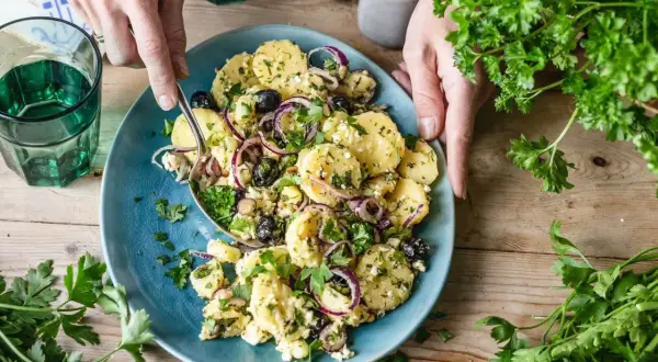 Ein köstlicher italienischer Kartoffelsalat mit Oliven, roten Zwiebeln und frischer Petersilie auf einem blauen Teller.