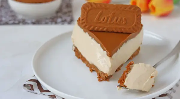 Una fetta di cheesecake Lotus, con biscotto e caramello, su un piatto bianco. Un morso su una forchetta.