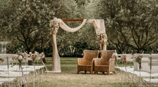 Un bel exemple de cérémonie laïque en plein air, avec un arche fleuri, des chaises blanches et deux fauteuils en rotin sous les oliviers.