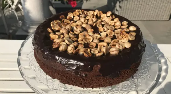 Czekoladowy tort z polewą i orzechami na szklanej paterze.