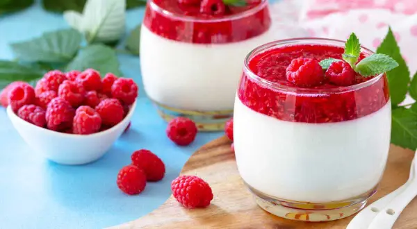 Deux panna cotta framboise, garnies de fruits rouges frais et de menthe, sur un plateau en bois.