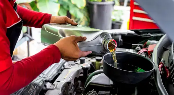 Mecánico vierte aceite nuevo en el motor de un coche, recordando que el aceite de coche caduca y debe cambiarse.
