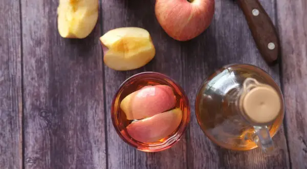 Ein Glas mit Apfelschnitzen und eine Flasche Apfelessig stehen bereit. Zeit, Apfelessig zu trinken!