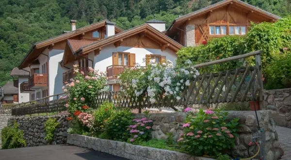 Case con balconi in legno e fiori colorati, incorniciate da un giardino rigoglioso. Un angolo di pace nel Val di Sole, dove si trova questo incantevole paesaggio.