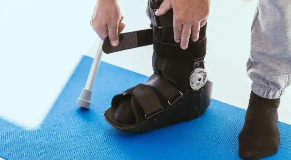 Persona si prepara a camminare con tutore caviglia, appoggiandosi a un bastone.