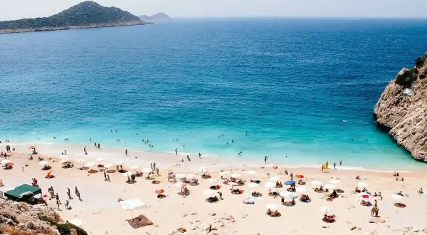 Piękna pogoda w Antalyi! Słoneczny dzień na plaży z turkusową wodą, ludźmi kąpiącymi się i odpoczywającymi pod parasolami.