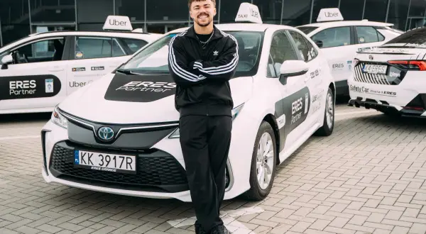 Młody kierowca Ubera z dumą pozuje przy białych autach. Zastanawiasz się, ile można zarobić w Uberze?