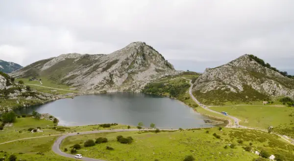 Paisaje montañoso con un lago sereno y carreteras sinuosas. Se puede ver gente disfrutando del **subir Lagos de Covadonga**.