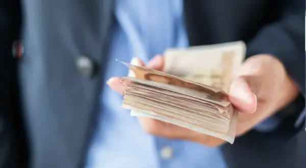 Dłoń trzymająca plik banknotów, ostrzeżenie przed oszustami w finansach dla ciebie.