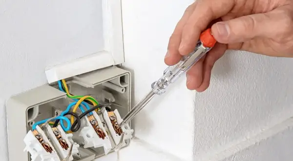 Ręka z próbnikiem napięcia sprawdza przewody w puszce elektrycznej. Dowiedz się, jak używać próbnik napięcia, by bezpiecznie pracować z instalacją.