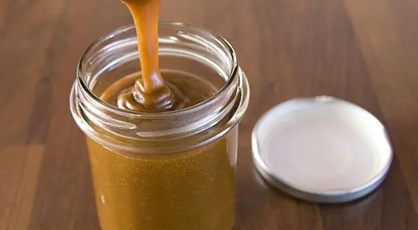 Caramel coulant versé dans un pot en verre, parfait pour une recette de pâte à tartiner noisettes maison.