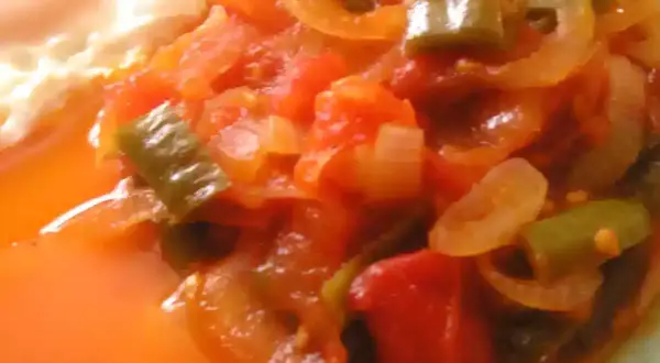 Une assiette de piperade recette, avec des poivrons verts, des oignons et des tomates mijotés, à côté d'un œuf au plat.