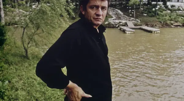 Johnny Cash, w czerni, stoi nad wodą. W jego oczach widać ból, jakby przeżywał coś trudnego, jak w piosence "Hurt".