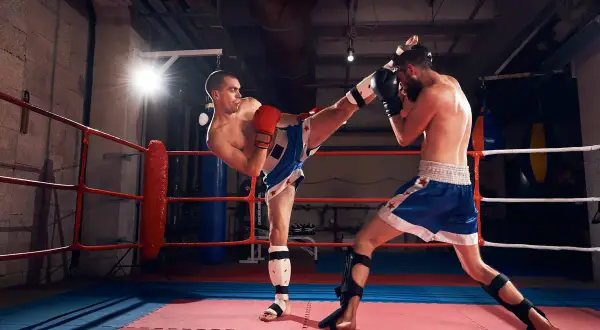 Two men are sparring in a boxing ring, demonstrating that sparring is a sport. One fighter delivers a powerful kick while the other defends.