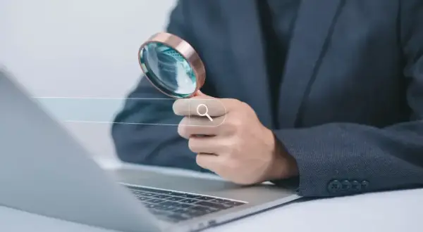 Dłoń z lupą nad polem wyszukiwania na laptopie. **Snr** szuka informacji.
