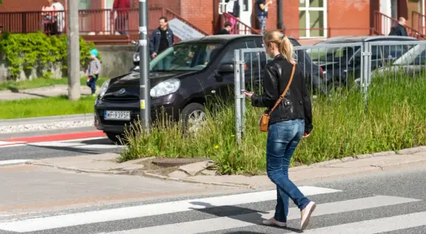Młoda kobieta, pieszy, idzie przez pasy, patrząc w telefon.