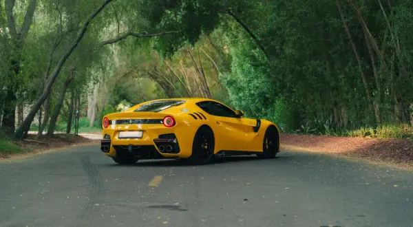 Żółte Ferrari F12 TDF sunie po leśnej drodze, otoczone bujną zielenią.