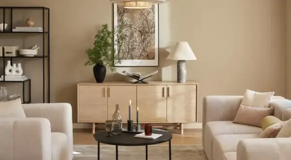 Jasny salon z beżową kanapą, drewnianą komodą i czarnym stolikiem kawowym.