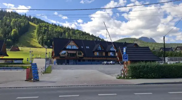 Parking pod Nosalem, z widokiem na górę i las. Restauracja z drewnianą elewacją, parking strzeżony.