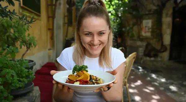 Uśmiechnięta kobieta prezentuje talerz z daniem, które wygląda jak pyszne dieta śródziemnomorska przepisy.