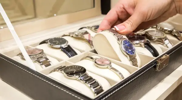 Una mano elige un reloj de una caja. Los relojes de pulsera, algunos de niquel que no se oxida, están ordenados en compartimentos.