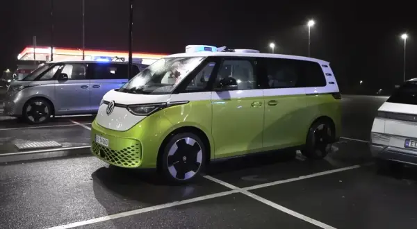 Zielony i srebrny VW ID. Buzz, jeden z niebieskimi światłami, parkuje nocą. Zasięg tych elektryków jest imponujący.