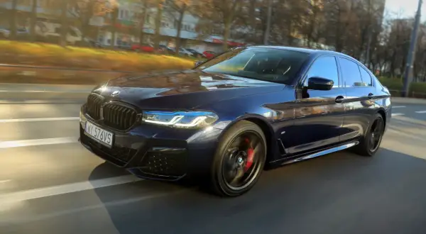 Ciemnoniebieskie BMW 540d w ruchu ulicznym, z widocznymi światłami LED i czerwonymi zaciskami hamulcowymi.