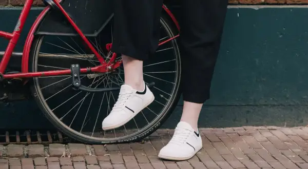 Voeten in witte barefoot schoenen naast een rode fiets. Nadelen barefoot schoenen: minder bescherming op oneffen ondergrond.
