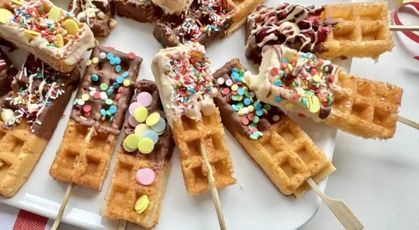 Bunte Waffeln am Stiel, getaucht in Schokolade und bestreut mit Streuseln und bunten Zuckerlinsen, laden zum Naschen ein.