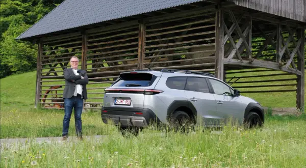 Man i kavaj står bredvid silverfärgad Toyota bz4x under ett gammalt träskjul.