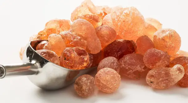 Grains ambrés de gomme arabique dans une cuillère métallique. Qu'est-ce que la gomme arabique ? Une résine naturelle aux multiples usages.