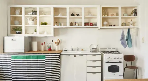 A cozy kitchen with open shelving displaying decorative items. A striped curtain hides the dishwasher, showcasing clever rental friendly upgrades.