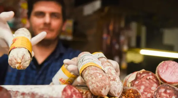 Un hombre con guantes blancos muestra varios tipos de salami, un embutido curado.