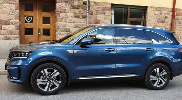 Blå laddhybrid diesel Kia Sorento parkerad framför en tegelbyggnad med en trädörr med ett hjärta.