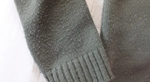 Zielony sweter z dzianiny, na którym widać mechacenie. Czy wiskoza się mechaci? Tak, ten materiał pokazuje oznaki zużycia.