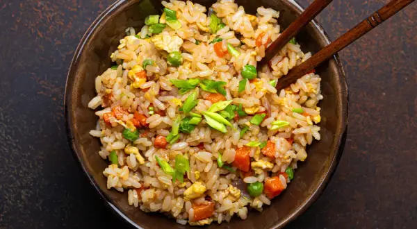 Un piatto fumante di riso alla cantonese ricetta originale, con piselli, carote, uova e cipollotto fresco, pronto per essere gustato con le bacchette.